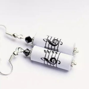 Könnte beinhalten: Ein Paar silberne Ohrringe mit schwarzen Perlen und weißen zylindrischen Anhängern mit Noten und Violinschlüsseln.