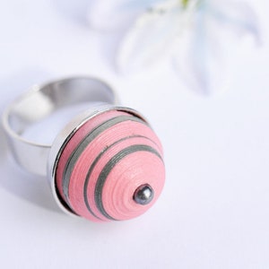 Könnte beinhalten: Ein silberner Ring mit einer pinkfarbenen und grauen Papier-Quilling-Kugel, die an der Ringschiene befestigt ist.