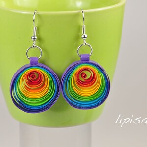 May include: Rainbow colored paper earrings with a purple backing and silver hooks. The earrings are shaped like circles and are made of multiple layers of paper.