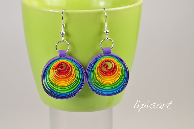 May include: Rainbow colored paper earrings with a purple backing and silver hooks. The earrings are shaped like circles and are made of multiple layers of paper.