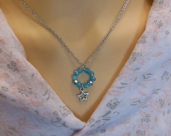 Peut inclure: Un collier argenté avec un pendentif composé d'un anneau de perles bleu clair et d'un petit charme en forme d'étoile argentée. Le collier est présenté sur un mannequin portant un haut rose à motifs floraux.