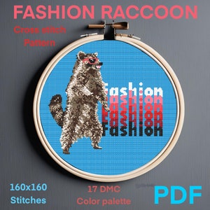 Puede incluir: Patrón de punto de cruz de un mapache con gafas de sol y la palabra "fashion" repetida en un degradado de rojo, rosa y negro. El patrón es de 160x160 puntos y utiliza 17 colores DMC. El patrón está disponible para descargar en PDF.