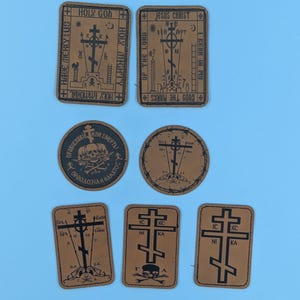 May include: A collection of brown leather patches with religious iconography. The patches feature crosses, text, and symbols like skulls. The text includes phrases like "Holy God" and "Jesus Christ". The patches are arranged on a light blue background.