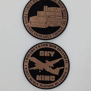 May include: Two circular black patches with copper-colored engravings. The top patch features a bulldozer and the text "SOMETIMES REASONABLE MEN MUST DO UNREASONABLE THINGS." The bottom patch shows an airplane, the text "SKY KING," and "I WOULDN'T KNOW HOW TO LAND IT, I WASN'T REALLY PLANNING ON LANDING IT."