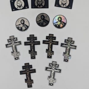 May include: A collection of eleven stickers featuring religious iconography. Three rectangular stickers, three circular stickers, and five cross-shaped stickers display depictions of Jesus Christ and the crucifixion with various metallic and black finishes.