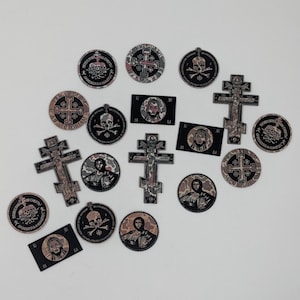 May include: A collection of circular, rectangular, and cross-shaped patches featuring religious and memento mori imagery. The designs include skulls, Orthodox crosses, and portraits of figures with text in Cyrillic and Latin scripts in black and white.