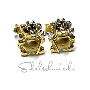 Könnte beinhalten: Ein Paar goldene und silberne Teufel-Ohrstecker. Die Ohrringe sind klein und zeigen einen Cartoon-Teufel mit Hörnern und einem Schwanz.