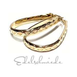 Könnte beinhalten: Ein Paar goldene Creolen mit einem detaillierten, gewebten Design. Die Ohrringe sind oval geformt und haben eine glatte, polierte Oberfläche.