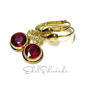 Könnte beinhalten: Ein Paar goldene Ohrringe mit roten Rubin-Edelsteinen. Die Ohrringe haben ein schlichtes, elegantes Design und sind perfekt für den Alltag.