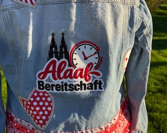 May include: A light blue denim jacket featuring a back patch with a black cathedral silhouette, a clock, and the text Alaaf Bereitschaft. The jacket is decorated with red and white striped and polka dot heart-shaped patches and a red polka dot skirt.
