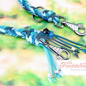 May include: A turquoise and blue braided dog leash with silver hardware and turquoise and blue tassels. The leash has a silver clasp and a silver ring. The leash is decorated with silver beads and stars. The text "Flechterei Rund um Hund" is visible in the image.