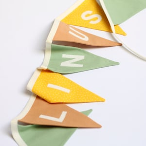 Könnte beinhalten: Ein Stoffbanner mit dem Wort "LINS" in weißen Buchstaben auf abwechselnd grünen, gelben und orangefarbenen dreieckigen Flaggen.