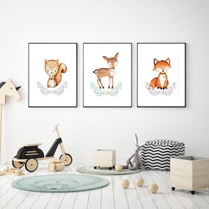 May include: Three framed watercolor prints featuring woodland animals: a squirrel, a deer, and a fox. Each animal is depicted in a cute, cartoon style, surrounded by floral accents. The prints are displayed in a bright, modern room with children's toys.