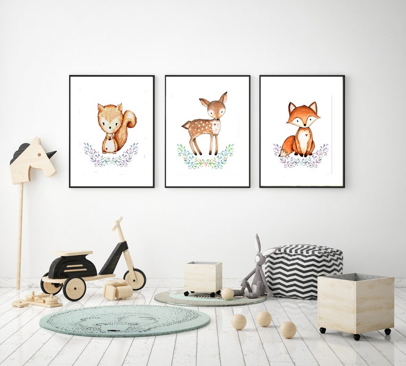 May include: Three framed watercolor prints featuring woodland animals: a squirrel, a deer, and a fox. Each animal is depicted in a cute, cartoon style, surrounded by floral accents. The prints are displayed in a bright, modern room with children's toys.