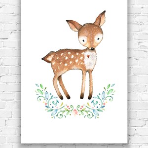 May include: Watercolor illustration of a fawn with brown fur and white spots, standing above a floral wreath. The fawn has large eyes and a small red heart on its chest. The artwork is printed on white paper and displayed on a white brick wall.