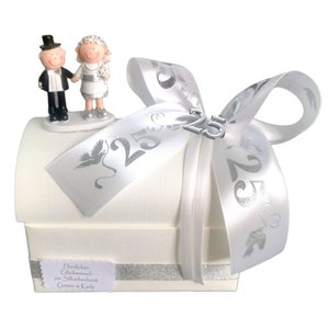 May include: A white gift box with a silver ribbon and a silver 25 charm. The box has a small figurine of a bride and groom on top. The box has a label that says "Herzlichen Gl&uuml;ckwunsch zur Silberhochzeit Gunter & Karla".