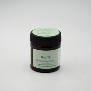 May include: A small, brown glass jar with a black lid. The jar contains a cream and has a label that reads "Hanf&ouml;l Gesichtspflegecreme" and "handmade NATURKOSMETIK www.naturkosmetik-hamstein.de".