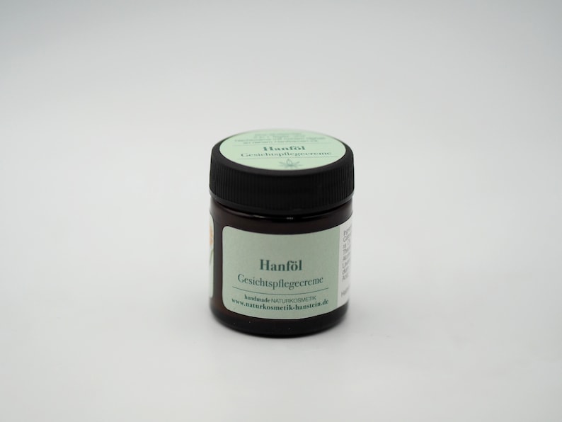 May include: A small, brown glass jar with a black lid. The jar contains a cream and has a label that reads "Hanf&ouml;l Gesichtspflegecreme" and "handmade NATURKOSMETIK www.naturkosmetik-hamstein.de".