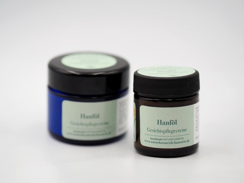 May include: Two small jars of face cream with green labels. The labels read "Hanf&ouml;l Gesichtspflegecreme" and "Hanf&ouml;l Gesichtspflegecreme". The jars are on a white surface.