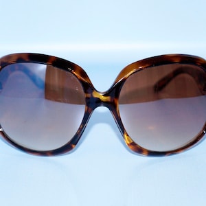 May include: Tortoiseshell sunglasses with brown lenses. The sunglasses have a large, rounded frame.