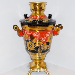 May include: An ornate samovar with a gold finish. The body is painted red with floral designs in yellow, white, and black. It has a spigot, handles, and a lid with black knobs. The samovar sits on a three-legged base.