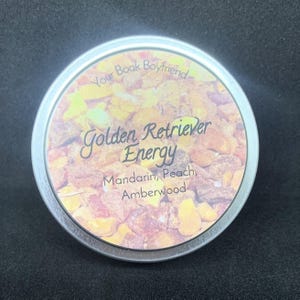 May include: A round, silver-colored tin with a label that reads "Your Book Boyfriend" and "Golden Retriever Energy." The label features the scent notes: Mandarin, Peach, and Amberwood. The tin is filled with small, amber-colored pieces.