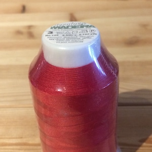 May include: A spool of red thread labelled "Aeroloce DERA 100% Polyester / полиэфир" with the text "No. 125 2,500m 2,750 yds Kernzwirn Overlock are spun кручёные армиров, нитки Filato per overlock Fil pour surjeteuse".