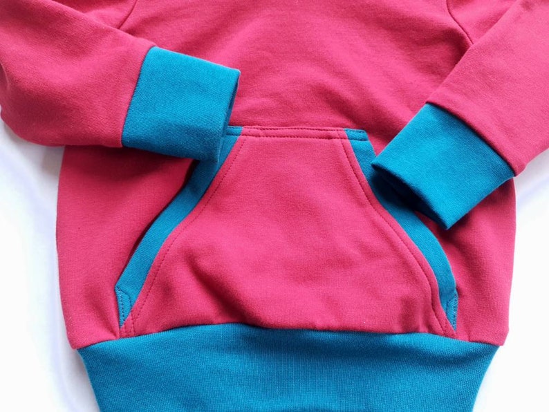 May include: A red hooded sweatshirt with teal blue trim around the cuffs and bottom hem. The sweatshirt has a single pocket on the front.