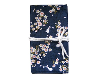 May include: A navy blue fabric journal with a floral and rabbit pattern. The design features white cherry blossoms and small white rabbits. A white rope is tied around the journal to keep it closed.