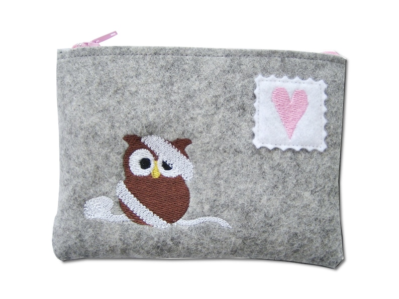 May include: A gray felt pouch with a pink zipper. The pouch features an embroidered brown owl with white accents and a small white square with a pink heart.