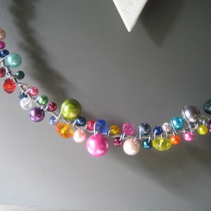 May include: A decorative garland or wreath element constructed from silver-toned wire twisted into a circular shape, adorned with a variety of multi-colored beads including pink, blue, green, yellow, red, and purple spheres and faceted crystals.