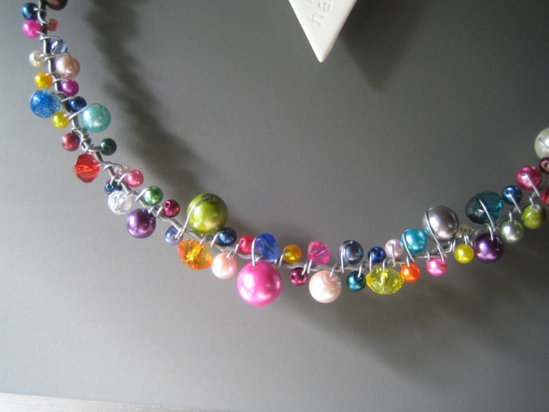 May include: A decorative garland or wreath element constructed from silver-toned wire twisted into a circular shape, adorned with a variety of multi-colored beads including pink, blue, green, yellow, red, and purple spheres and faceted crystals.