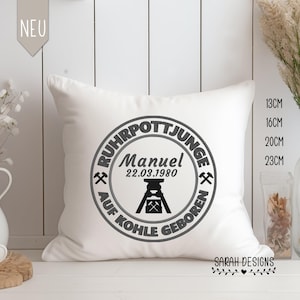 Puede incluir: Almohada blanca con un diseño circular negro y gris que dice "Ruhrpottjunge" con un símbolo minero y el texto "Manuel 22.03.1980 Auf Kohle Geboren".