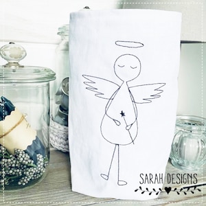 Könnte beinhalten: Ein weißes Geschirrtuch mit einem schwarzen gestickten Strichmännchen-Engel, der einen Stern hält. Der Engel hat einen Heiligenschein und Flügel. Der Text "SARAH DESIGNS" ist unten auf das Handtuch gestickt.