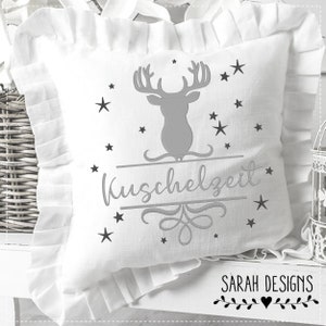 May include: White pillow with a gray embroidered deer, stars, and the text "Kuschelzeit". The pillow has a ruffled edge and is on a white surface.