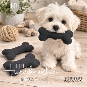 May include: A fluffy white dog holds a dark gray bone-shaped dog toy in its mouth. Two additional gray dog bones are on the wooden surface. The image includes the text "ITH Hundeknochen AB 18x13 5 Größen" and the Sarah Designs logo.