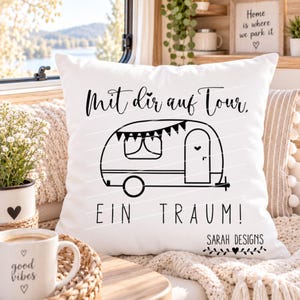 Könnte beinhalten: Ein weißes quadratisches Kissen mit einer schwarzen Strichzeichnung eines Wohnwagens mit Wimpelkette. Der Text lautet Mit dir auf Tour, EIN TRAUM! sowie Sarah Designs mit einem kleinen Herzsymbol. Das Motiv ist mittig auf dem Kissen platziert.