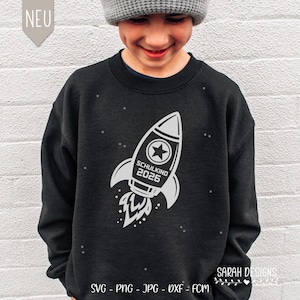 Könnte beinhalten: Schwarzes Sweatshirt mit weißem Raketen-Design. Die Rakete hat einen Stern und den Text "SCHULKIND 2026". Das Sweatshirt hat einen Rundhalsausschnitt.