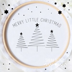 Op de afbeelding: Een witte borduurring met de tekst "Merry Little Christmas" en drie gestileerde zwarte kerstboompjes. De ring is omgeven door kleine zwarte sterretjes.