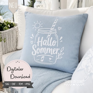 Op de afbeelding: Een lichtblauw vierkant kussen met een witte afbeelding van een pot, zon en de woorden "Hallo Sommer". Het kussen ligt op een witte rieten stoel met een blauwe deken. De woorden "Digitaler Download" zijn ook zichtbaar.