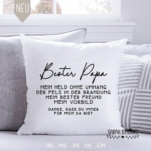 May include: White square throw pillow with black script text that reads "Bester Papa" and other German text. The pillow is on a couch with other pillows. The pillow has a "NEU" tag in the upper left corner.