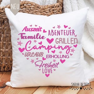 Könnte beinhalten: Weißes Kissen mit rosa gesticktem Text in Herzform. Der Text lautet "Auszeit Familie Abenteuer Grillen Camping Urlaub Erholung Freiheit Love".