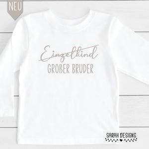 Könnte beinhalten: Weißes Langarmshirt mit dem durchgestrichenen Text "Einzelkind" und dem Text "Grober Bruder" darunter. Das Shirt hat einen braunen Druck.