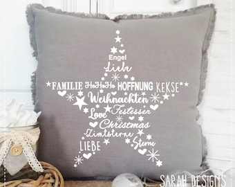 May include: Gray throw pillow with a white Christmas tree design. The tree is made up of words like "love", "family", "Christmas", and "hope". The pillow has a frayed edge and the words "SARAH DESIGNS" are printed at the bottom.