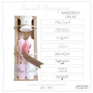Könnte beinhalten: Eine Holzgeschenkbox mit zwei Kerzen, einem weißen Keramikbehälter und Trockenblumen. Die Kerzen sind rosa und weiß, mit floralen Designs und dem Text "Alles Gute" und "Von Herzen". Die Box ist mit Bindfaden und einem Band gebunden.
