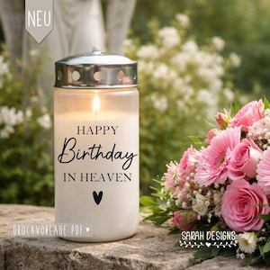Op de afbeelding: Een brandende witte kaars met de woorden "HAPPY Birthday IN HEAVEN" in zwart schrift, een zwart hart en een zilveren deksel. Rechts staat een boeket roze rozen en groen. Het woord "NEU" staat linksboven.