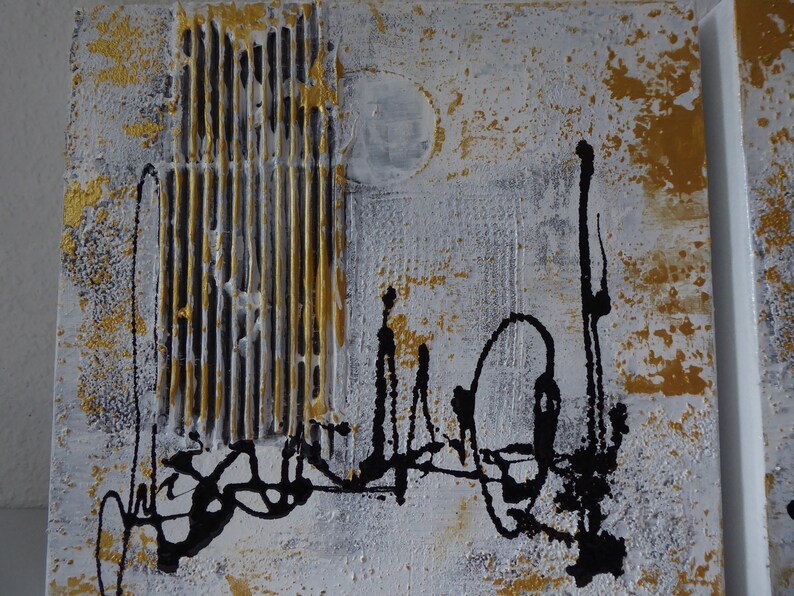K&ouml;nnte beinhalten: Abstrakte Kunstmalerei auf Leinwand mit einem strukturierten goldenen und wei&szlig;en Hintergrund. Schwarze Linien und Formen sind auf die Leinwand gemalt.