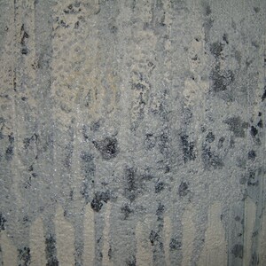 May include: A close-up of a textured, gray surface with white paint streaks. The surface has a rough, uneven texture and appears to be made of concrete or plaster.