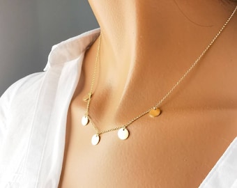 May include: A gold necklace with five small round pendants. The necklace is on a model wearing a white shirt.
