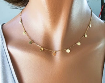 May include: A gold chain necklace with small round charms hanging from it. The necklace is on a model's neck.